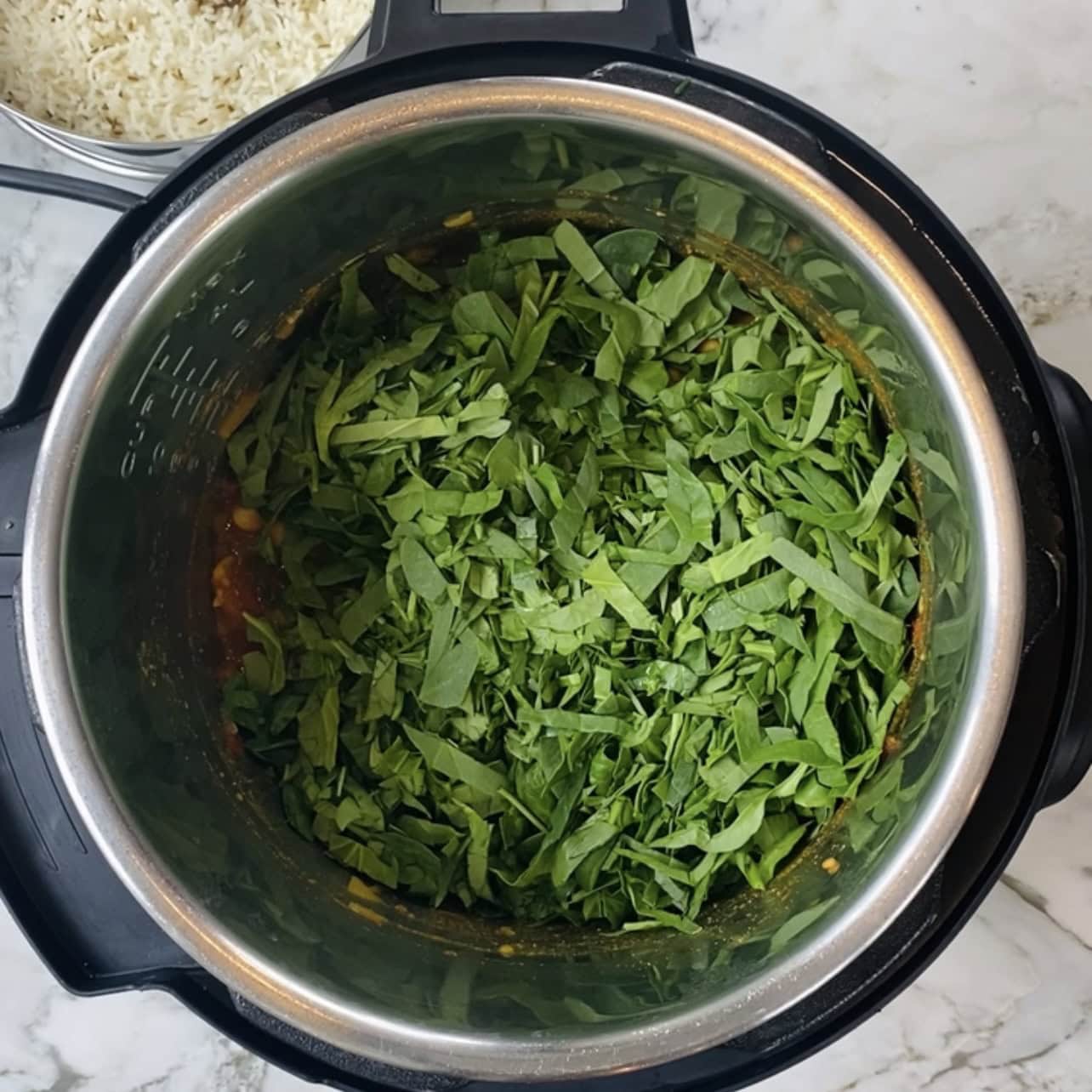 Chopped spinach added to an Instant Pot chana saag with other ingredients visible underneath, and a separate dish of cooked rice in the background.