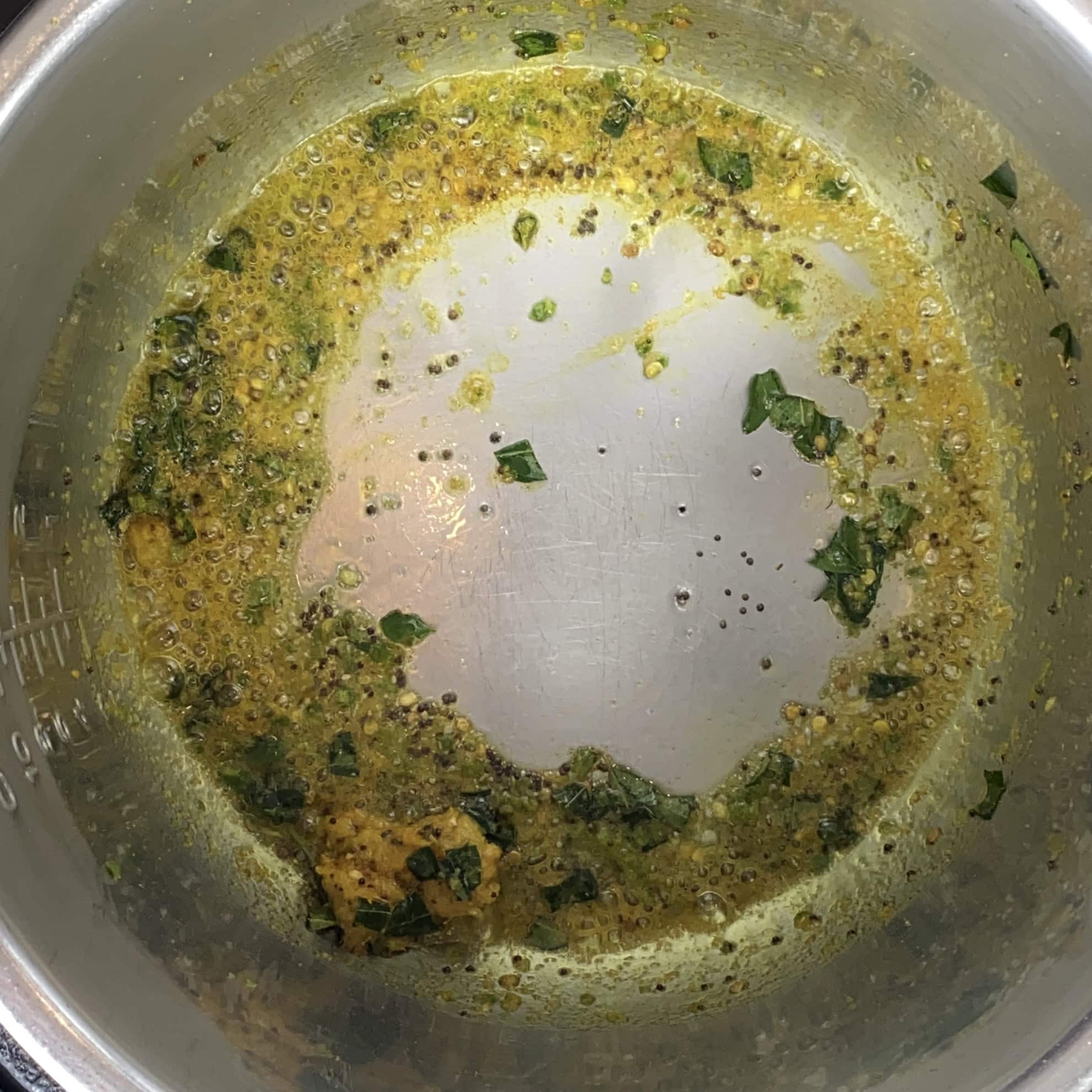 A metal pot with a yellow-green spice mixture, sautéed with herbs and bubbles, leaving some of the pot surface visible in the center.
