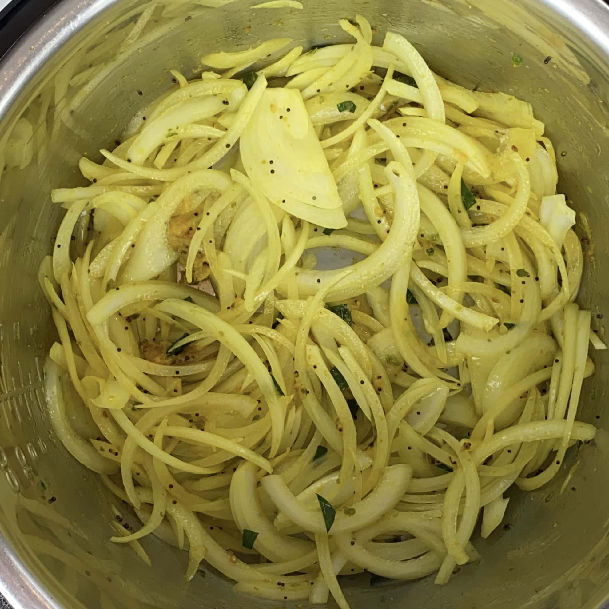 Sliced onions with turmeric and spices cooking in a stainless steel pot.