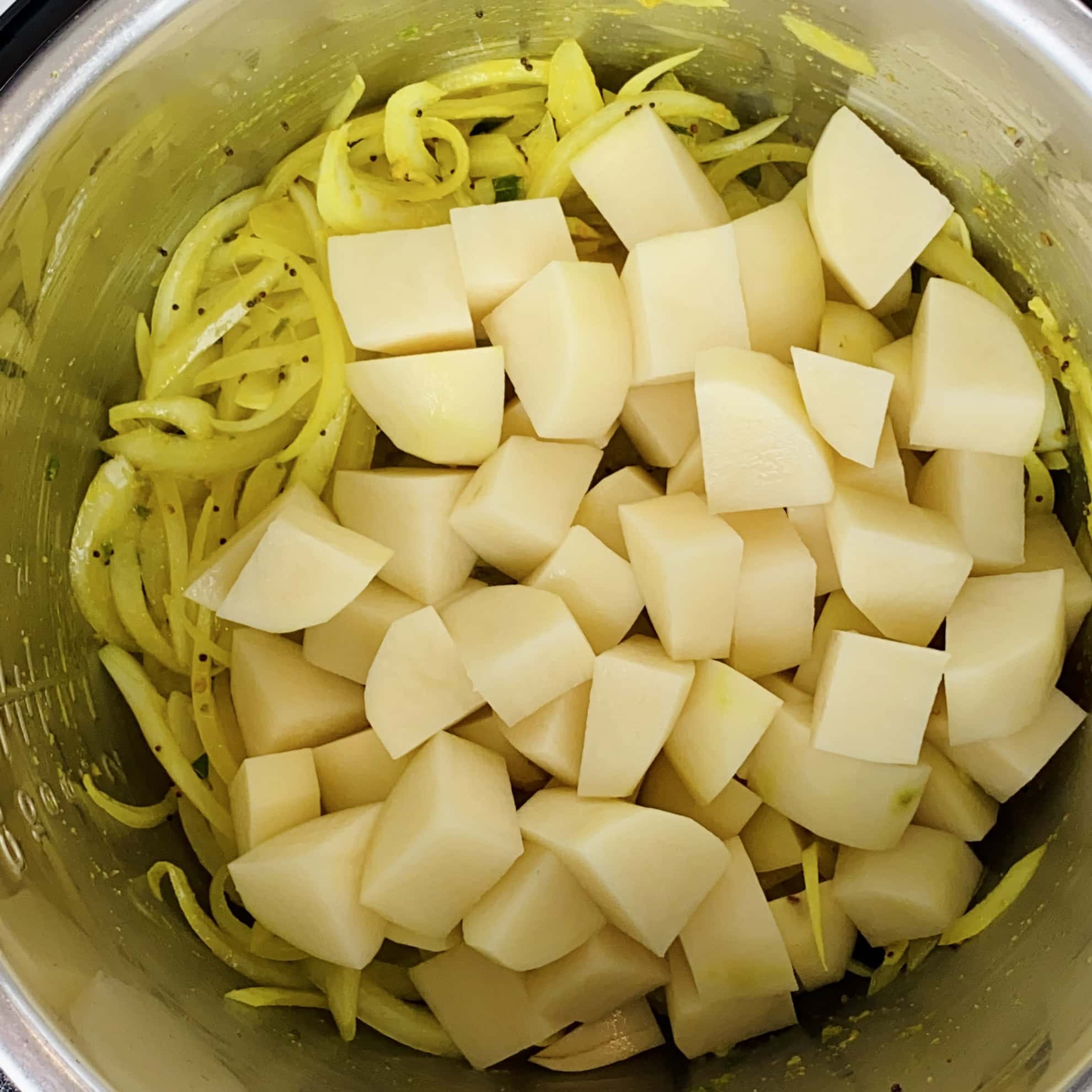 Diced potatoes and spiralized yellow onions in a stainless steel pot, seasoned with spices.