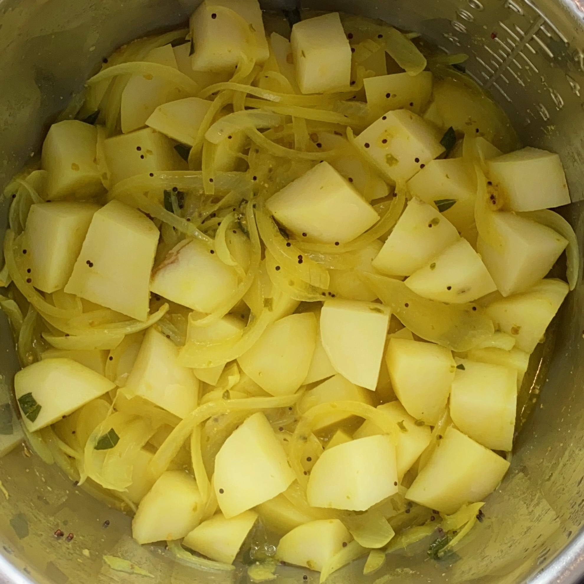 Cubed potatoes and sliced onions mixed with spices in a stainless steel pot.