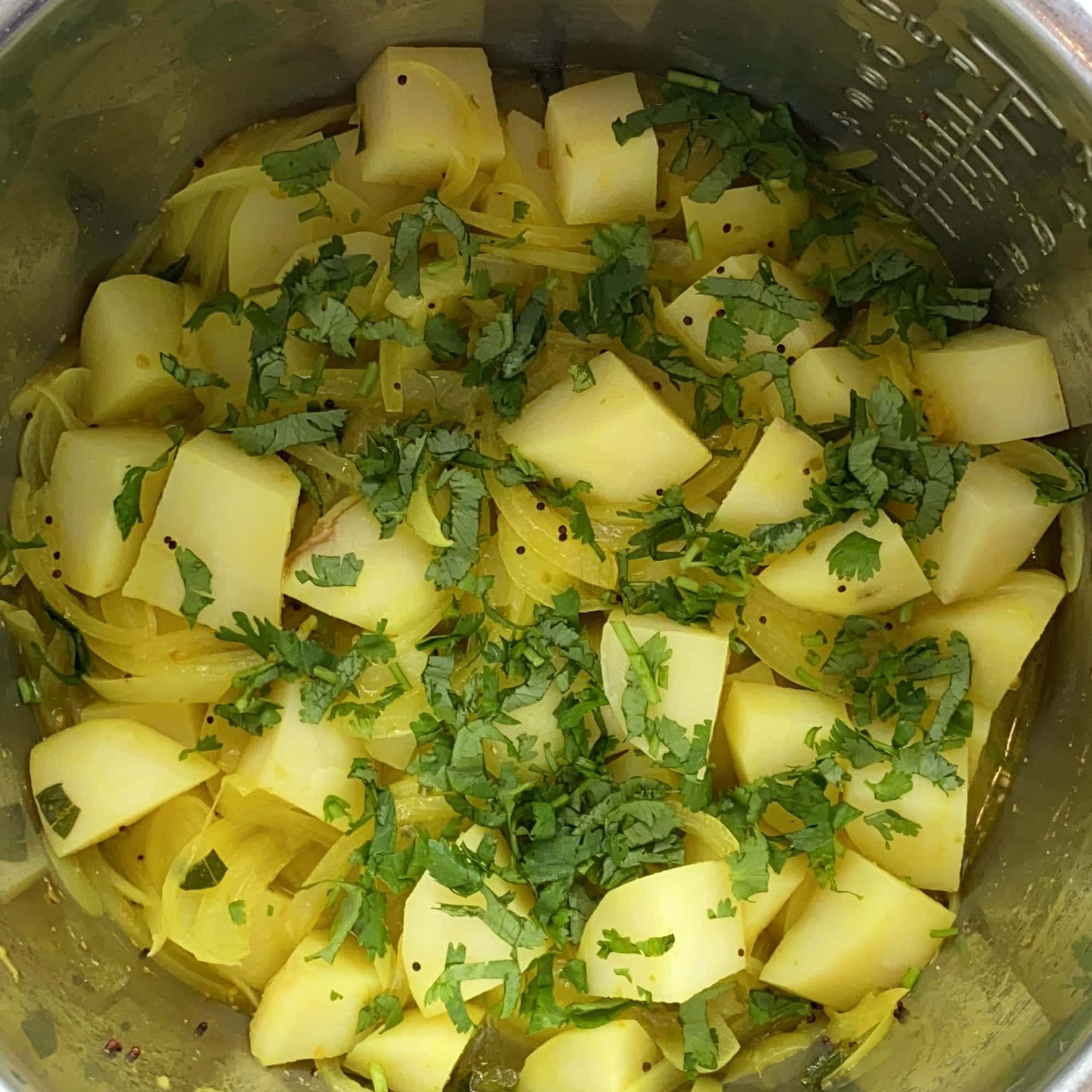 Diced potatoes and sliced onions cooked with spices, garnished with chopped cilantro, in a stainless steel pot.