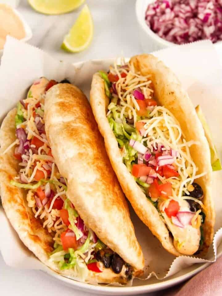 2 chalupas served in a white bowl topped with lettuce, tomatoes and cheese