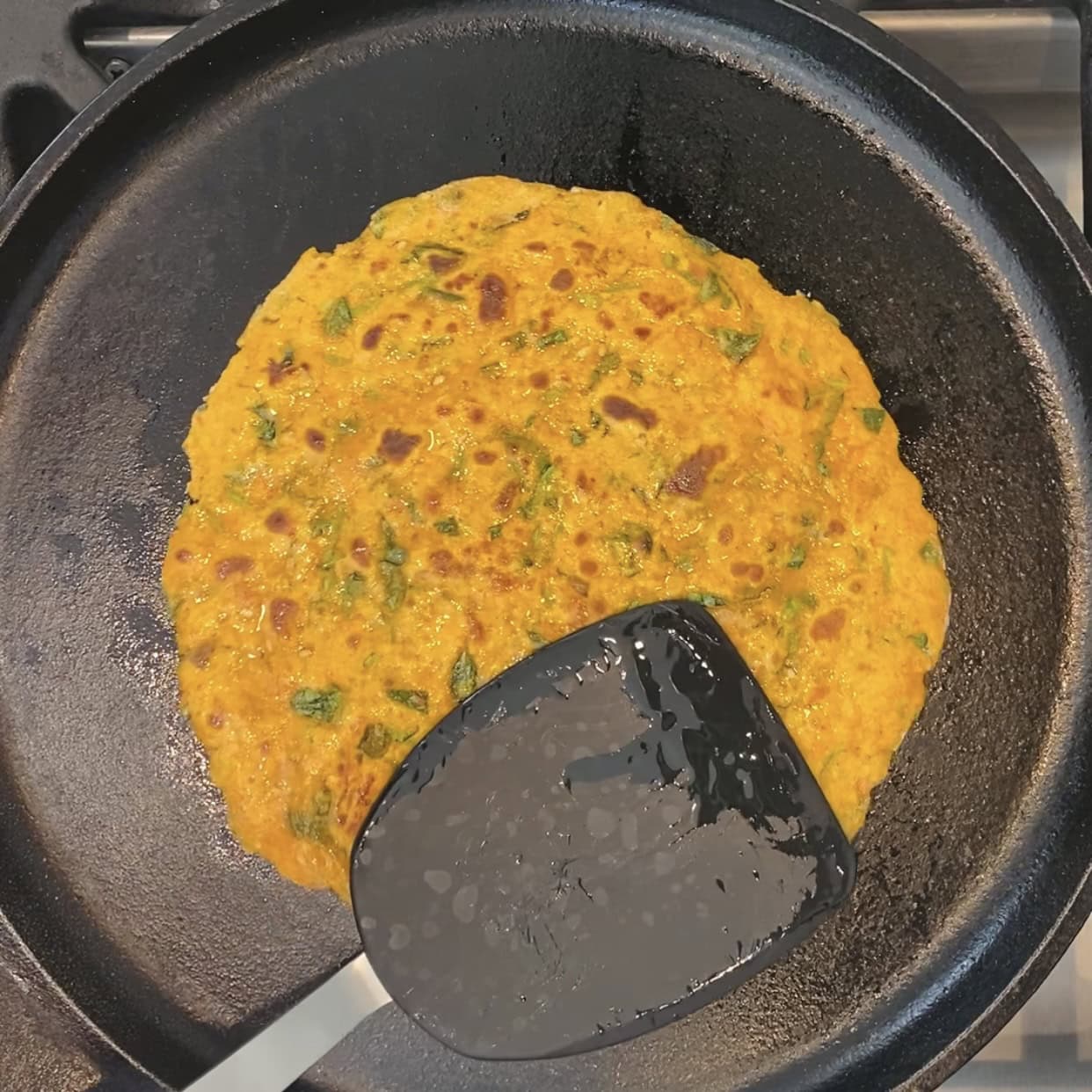 pressing methi thepla with a spatula while cooking. 
