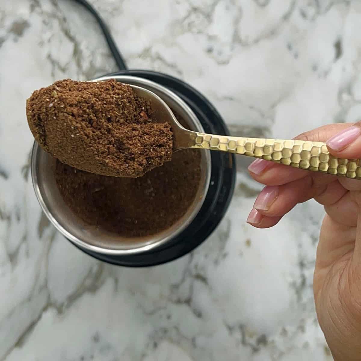 Garam masala in a spoon over the spice grinder 