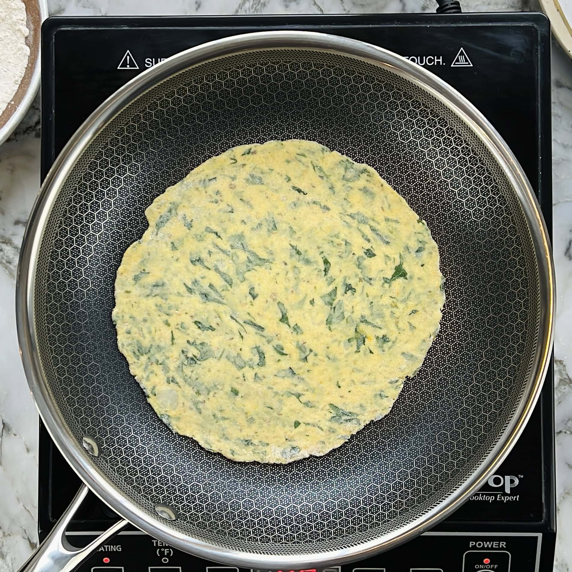 A round, kale potato flatbread cooks in a nonstick frying pan on an induction cooktop.