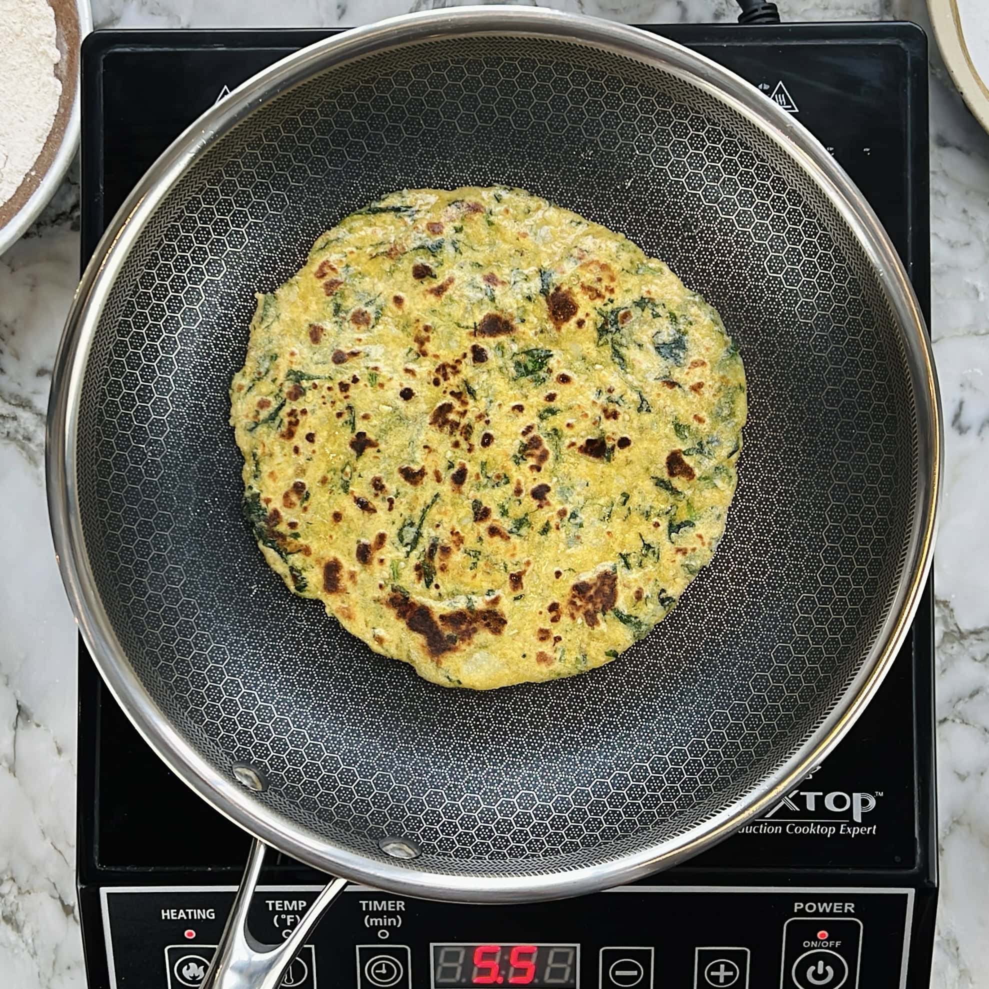 A kale aloo paratha cooks in a frying pan on an induction cooktop.