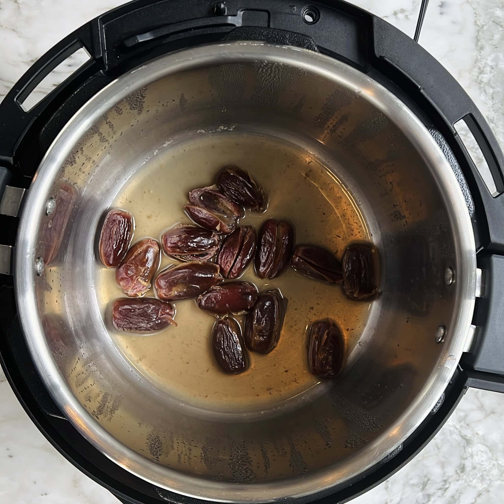 Pitted dates and liquid in the inner pot of an electric pressure cooker, viewed from above.
