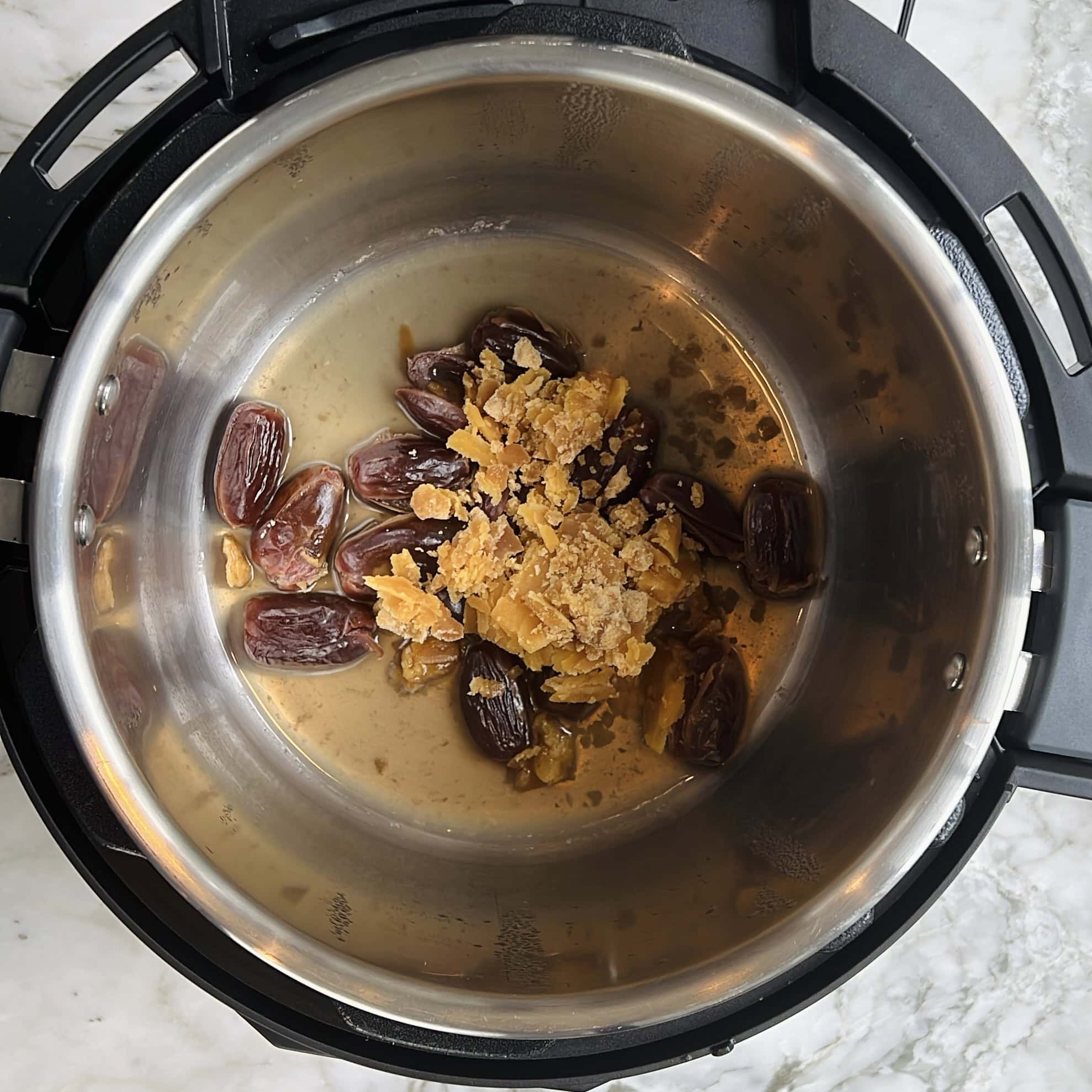 An overhead view of an Instant Pot containing whole dates and crumbled jaggery on its metal base.