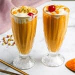 Mango Mastani served in two tall glasses garnished with nuts