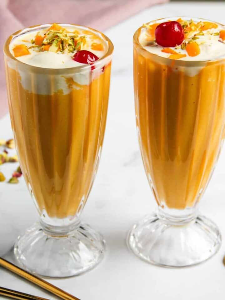 Mango Mastani served in two tall glasses garnished with nuts