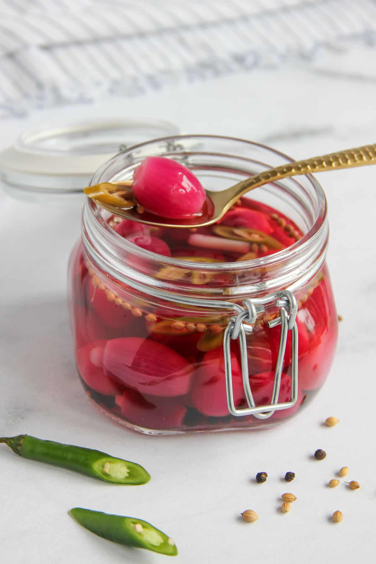 pickled pearl onions in a glass jar with a gold spoon