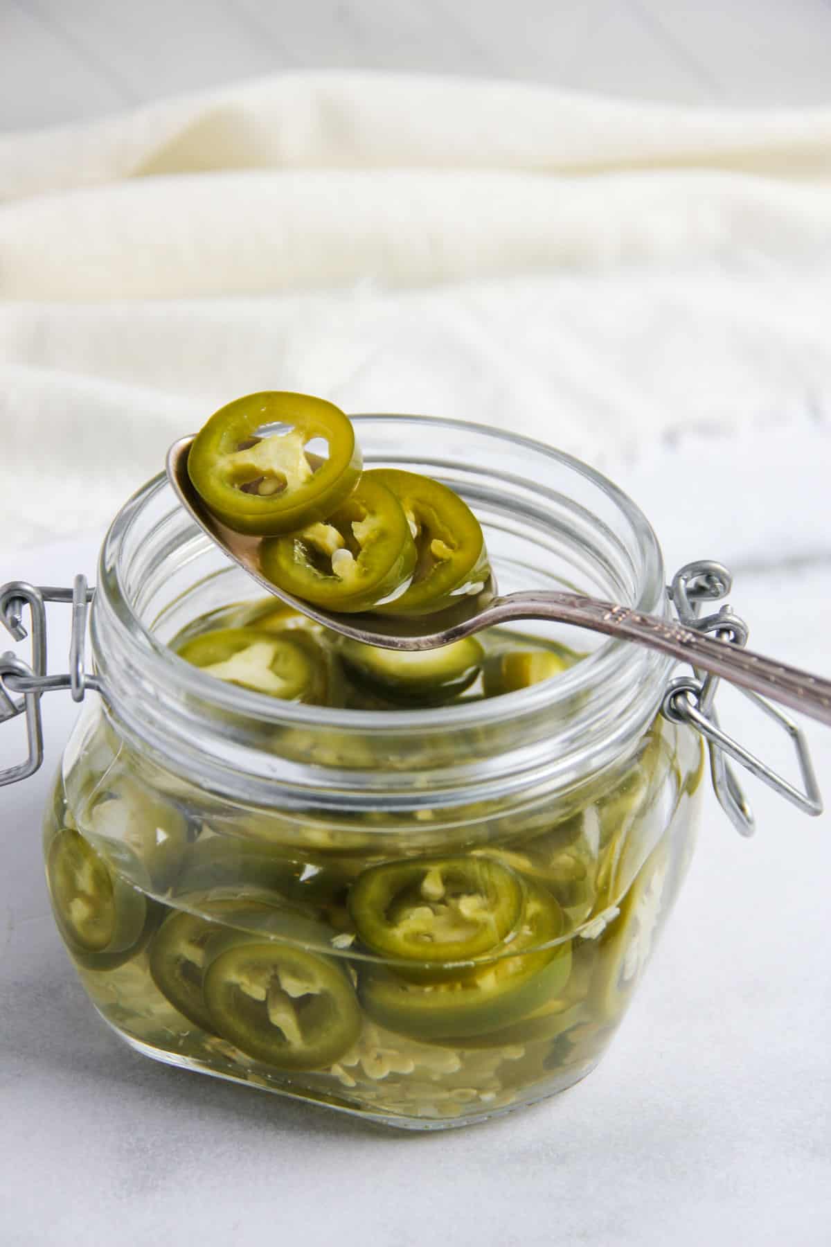 Pickled jalapenos in spoon over a glass jar 