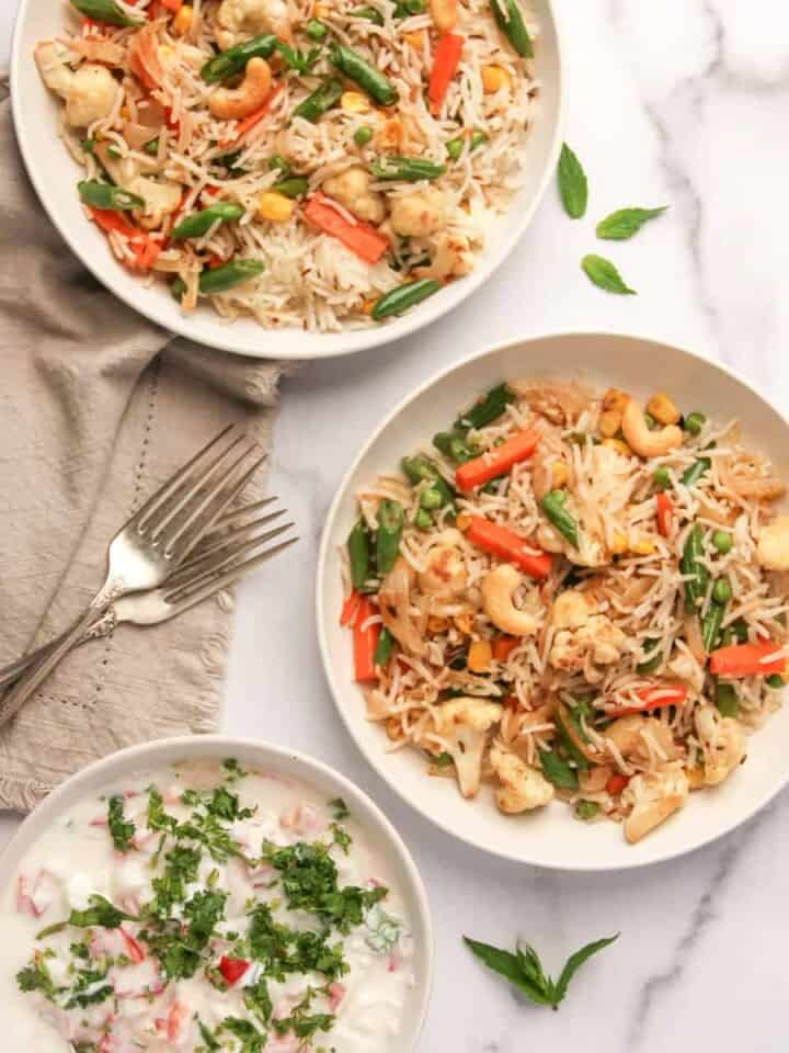 veg pulao in 2 white serving bowls with raita on the side