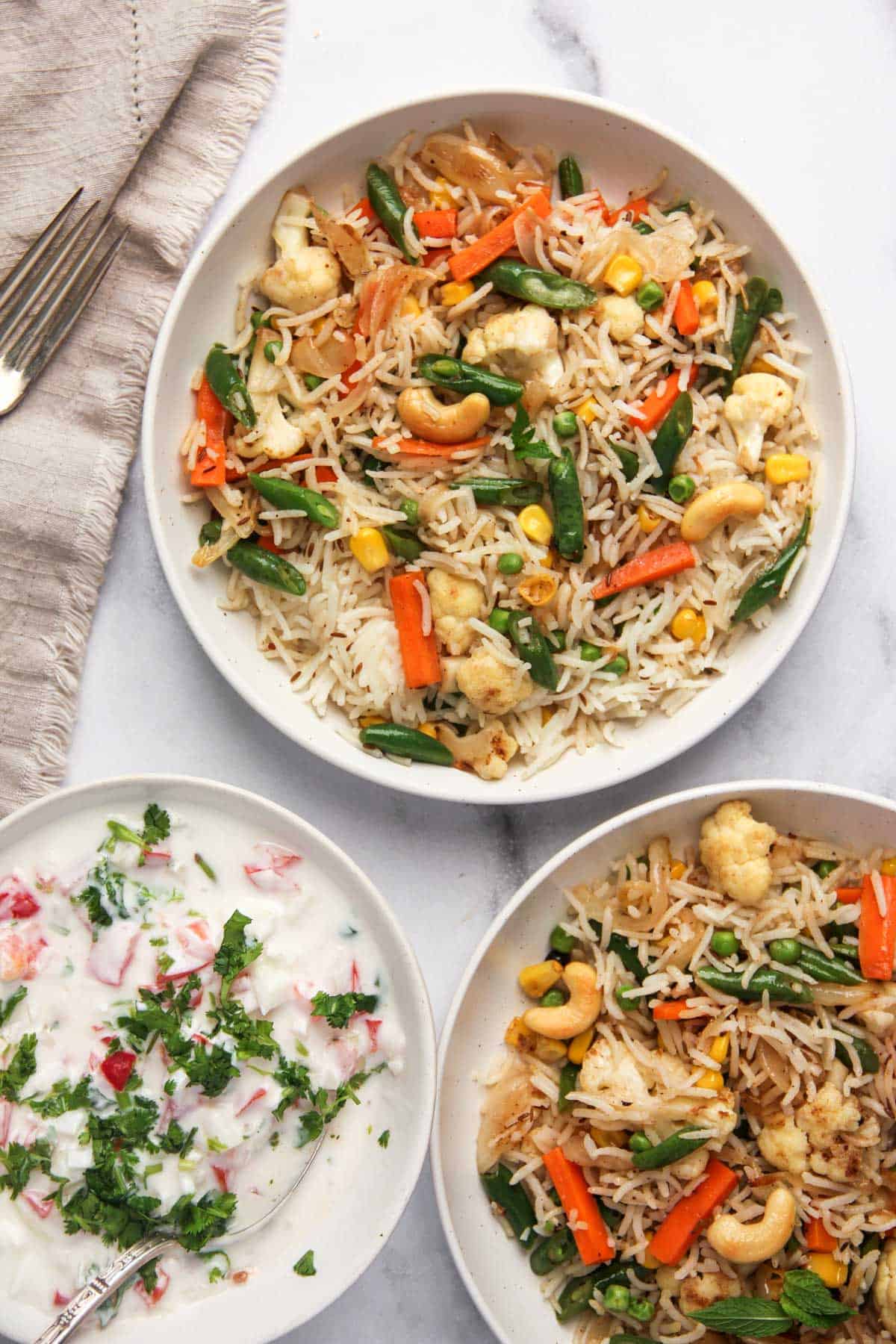 veg pulao in 2 white serving bowls with raita on the side