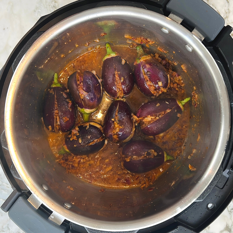 Stuffed eggplants cooked in a spiced sauce inside a pressure cooker, viewed from above.