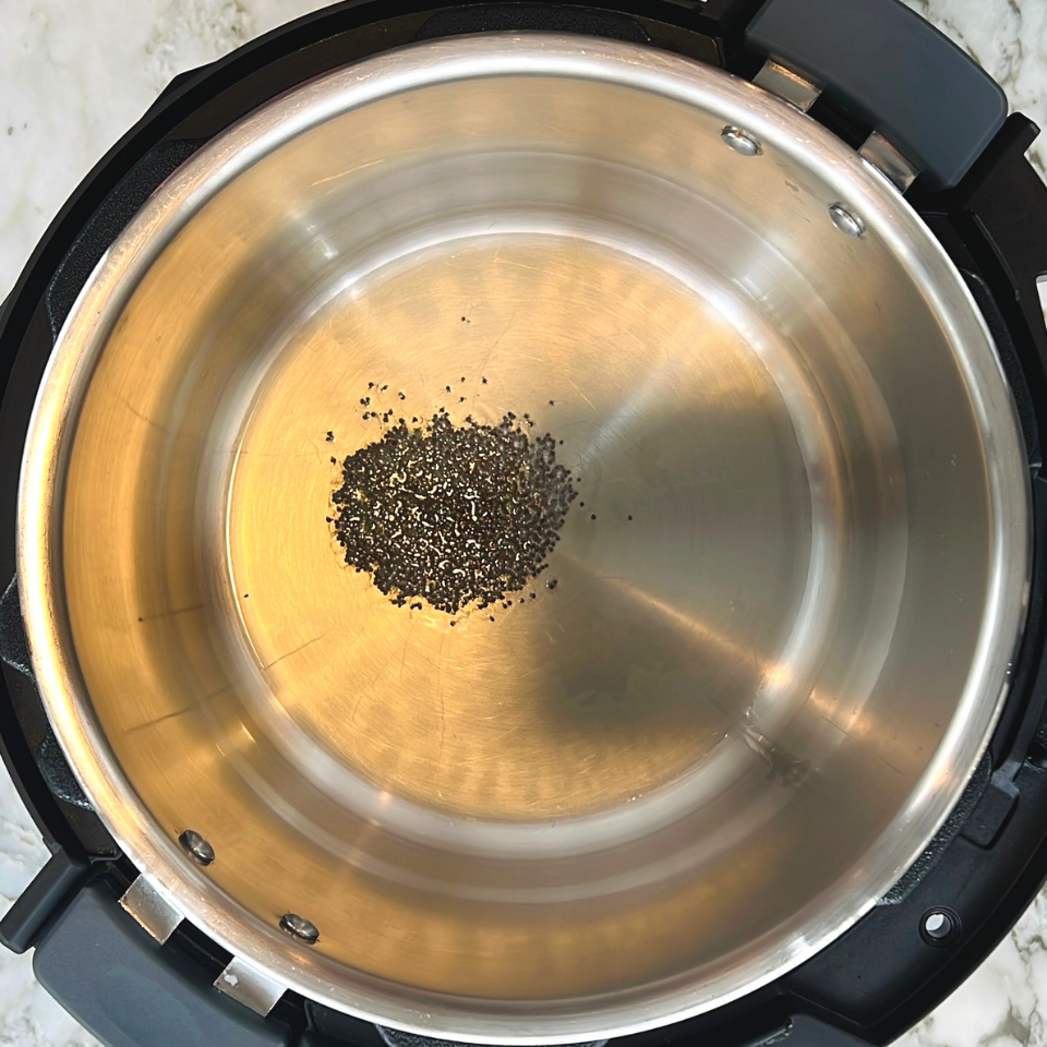 Whole black peppercorns scattered in the center of a stainless steel pot on a marble countertop.