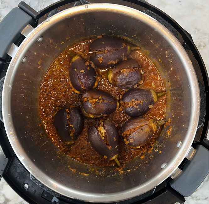 Whole eggplants cooked in a spiced tomato and onion sauce inside a stainless steel Instant Pot on a marble countertop.