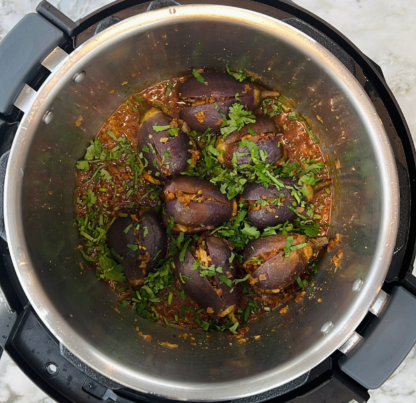 Stuffed eggplants cooked in a spiced tomato sauce, garnished with chopped cilantro, inside a stainless steel pressure cooker.