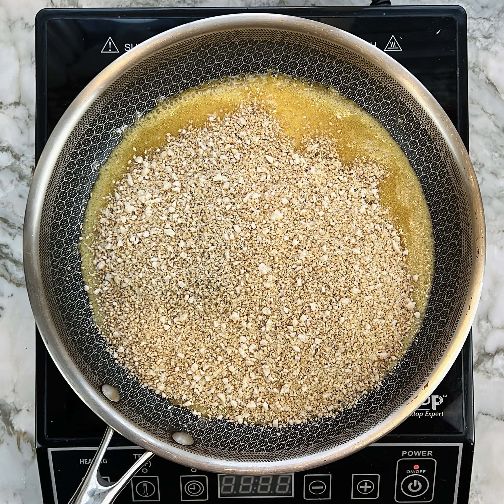 Ground sesame seeds mixture added to melted jaggery in a nonstick pan.