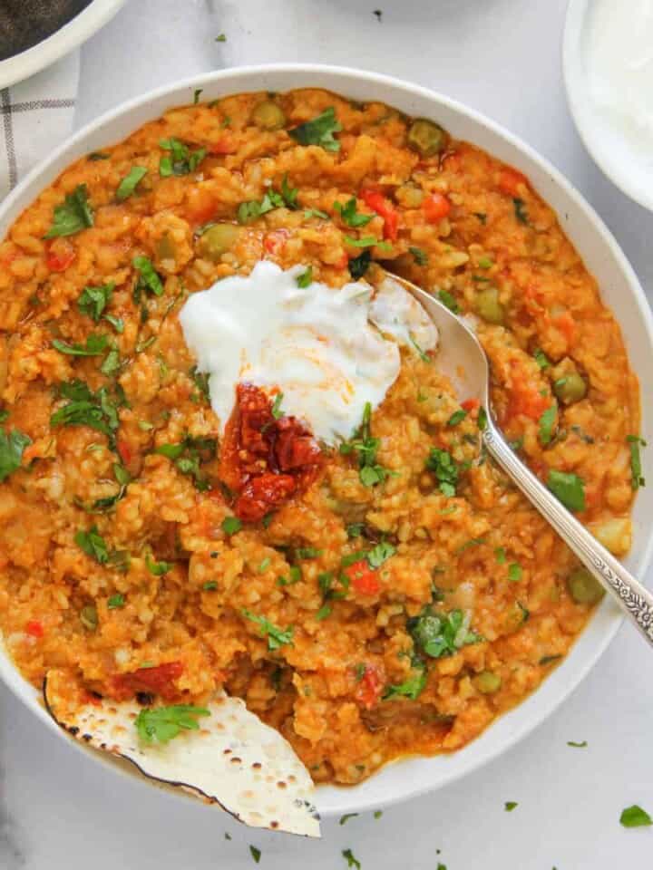 khichdi served in a white bowl with yogurt and pickles