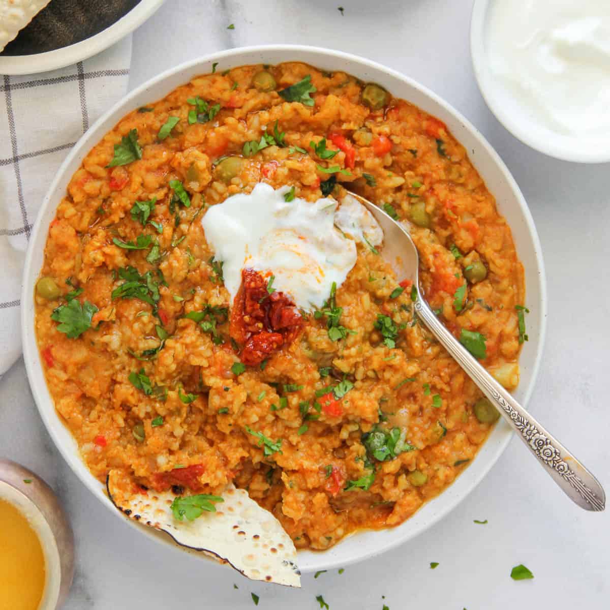 khichdi served in a white bowl with yogurt and pickles