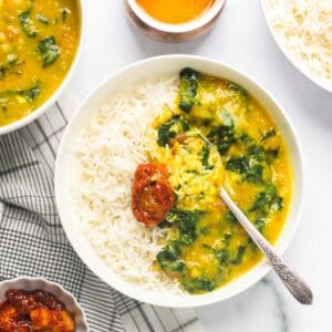 spinach dal served with rice and pickle in a white bowl