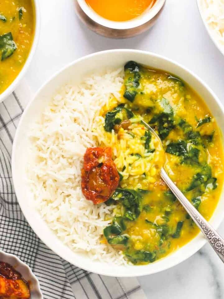 spinach dal served with rice and pickle in a white bowl
