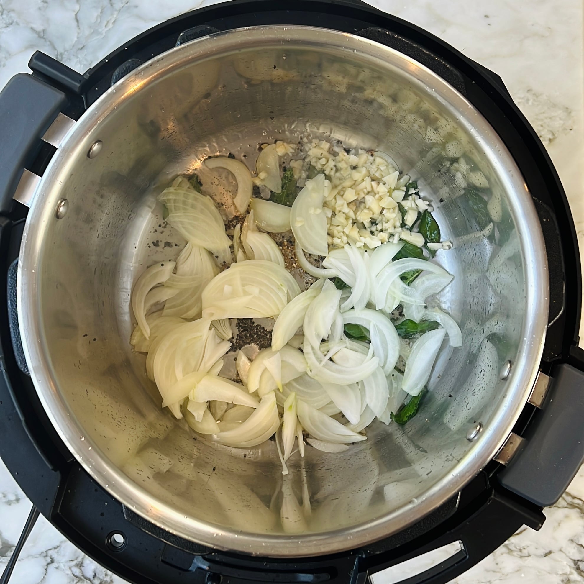 Sliced onions, chopped garlic, and green chilies sautéing with spices in a Instant Pot insert.