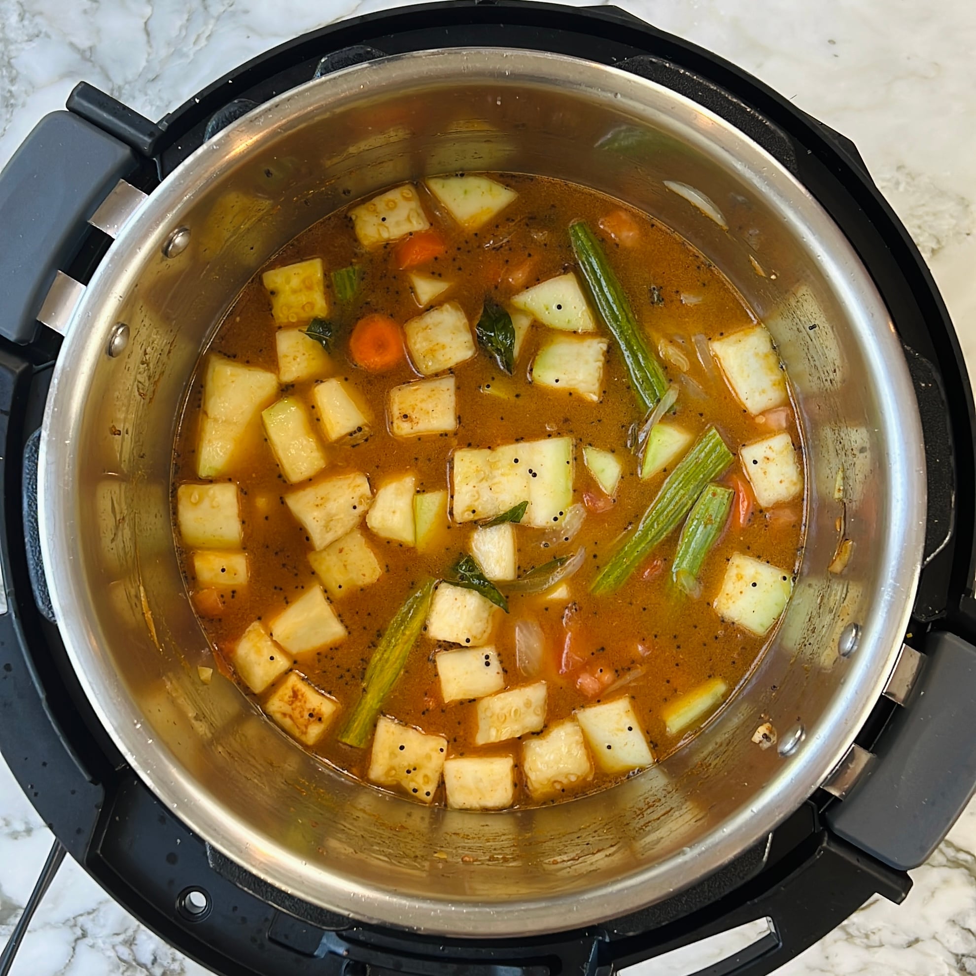 Diced vegetables, lentils and spices cooking in an Instant Pot on a marble countertop.