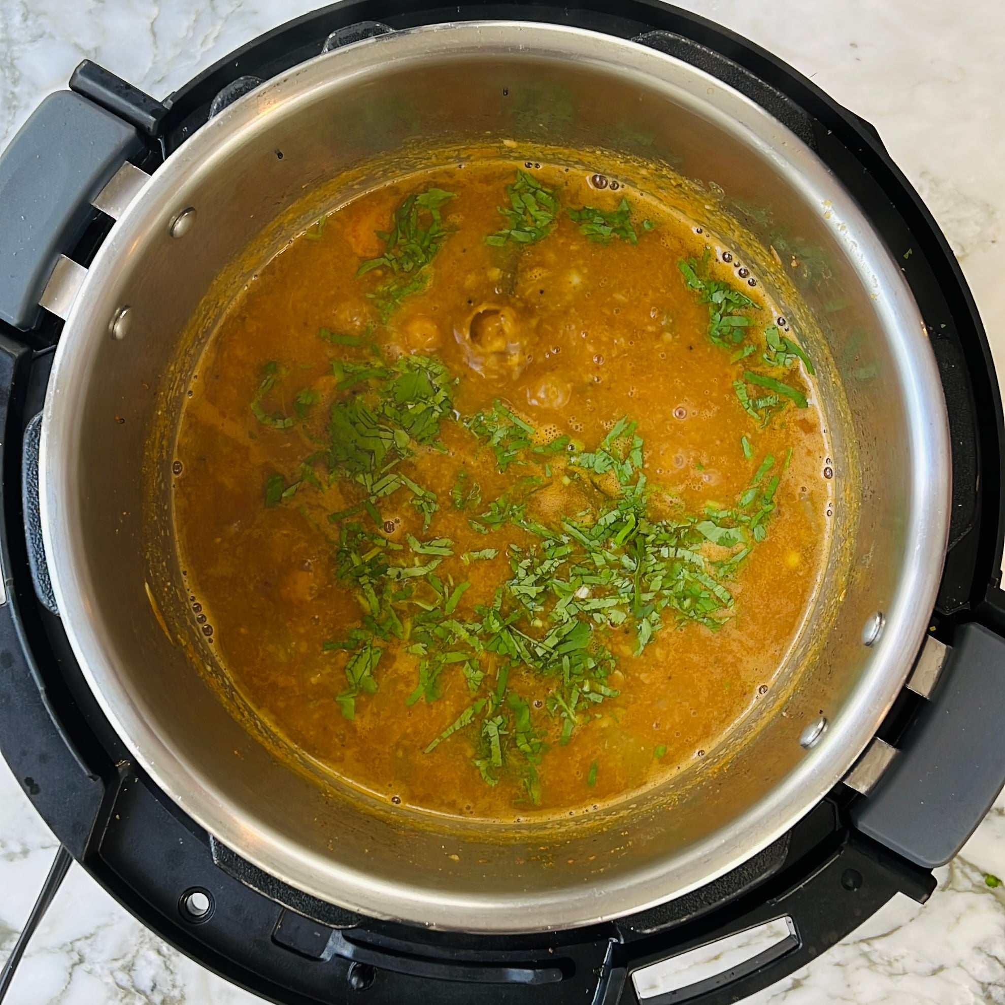 Sambar garnished with chopped cilantro, cooked in an electric pressure cooker on a marble countertop.
