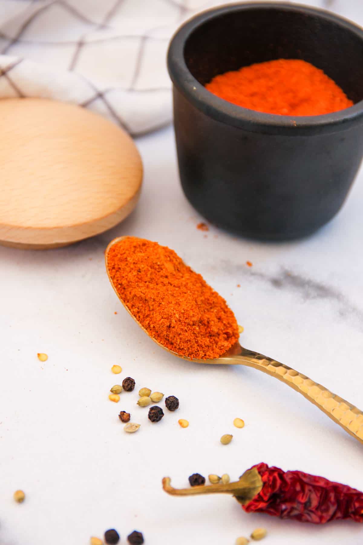 sambar powder in a spoon next to a jar and whole spices 