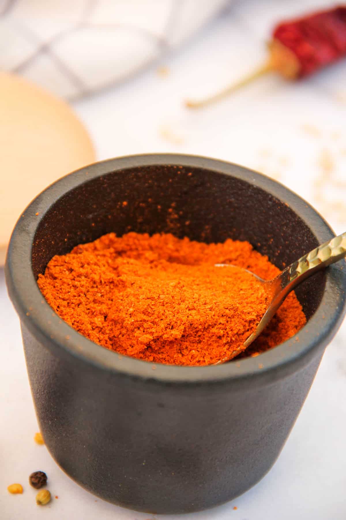 sambar powder in a black cup with a gold spoon 
