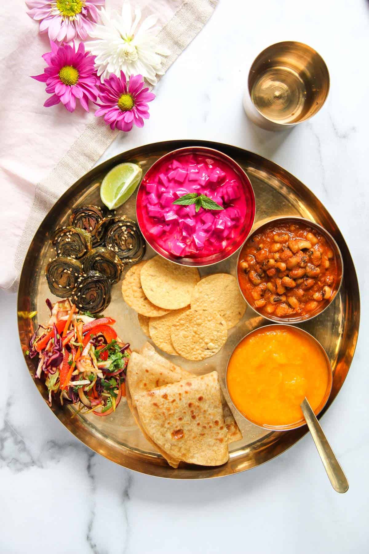 Vegetarian Thali with beet raita, black eyed peas curry, aamras, chapati, cabbage salad and patra