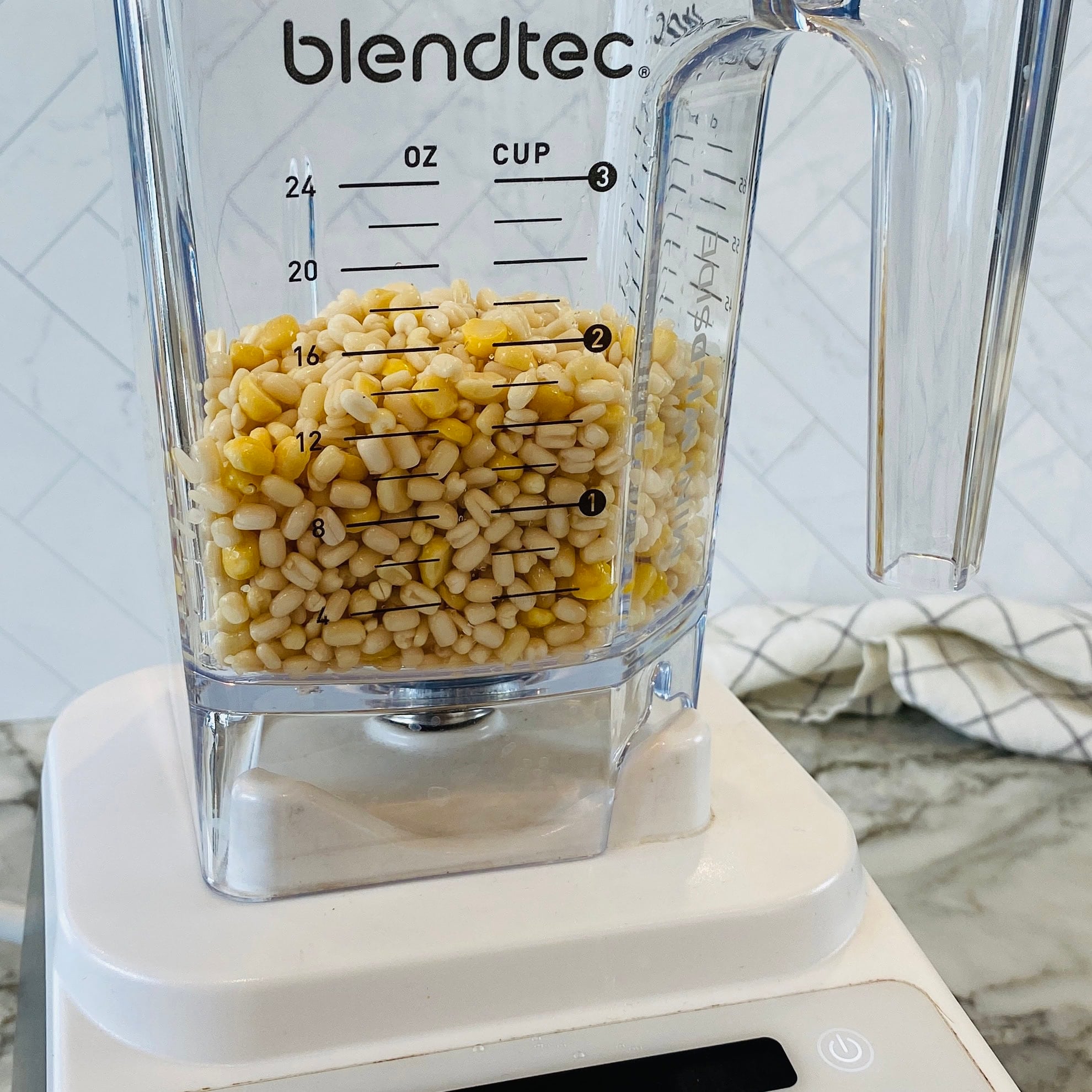 A Blendtec blender filled with white and yellow lentils sits on a kitchen counter.