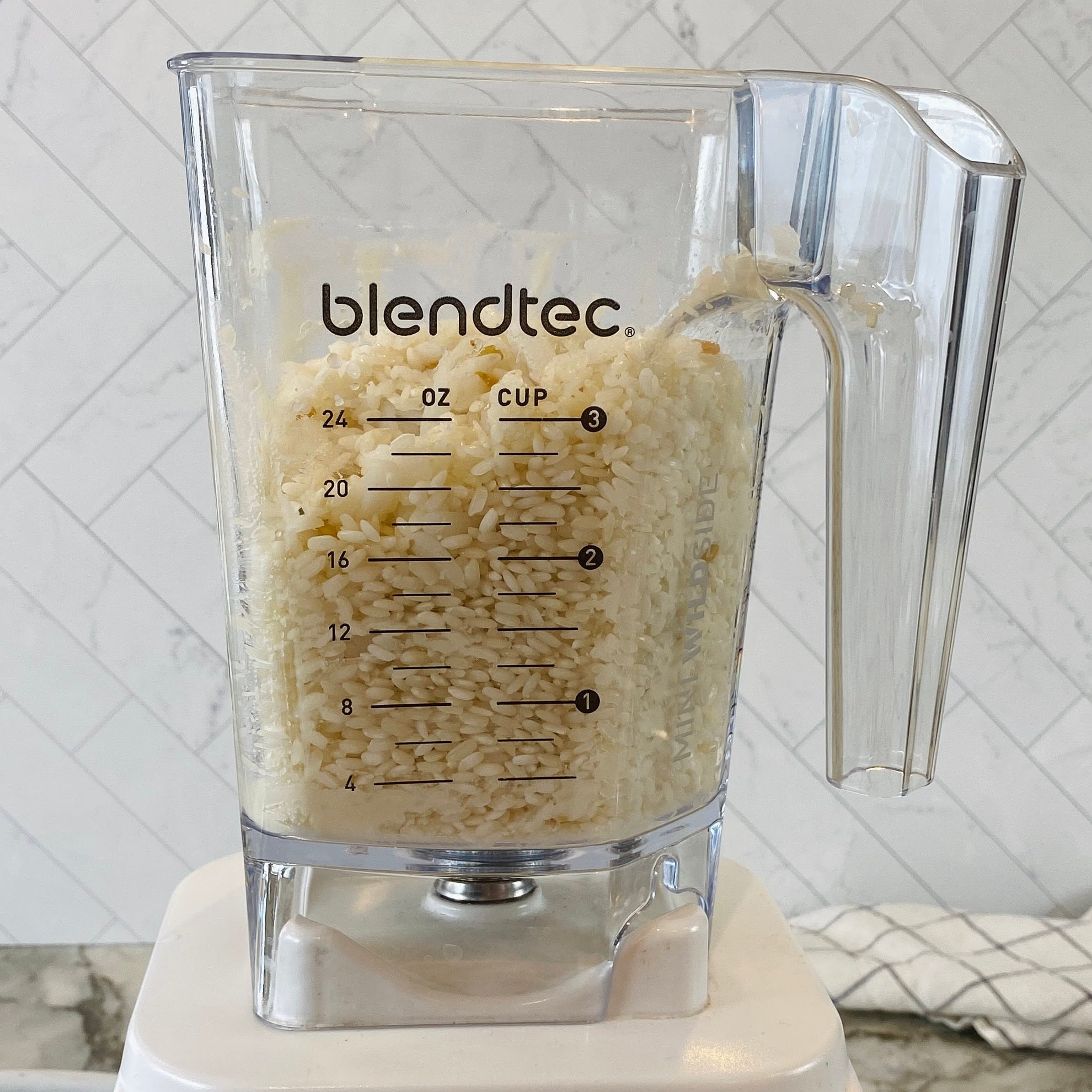 A Blendtec blender jar filled with soaked rice placed on a blender base.