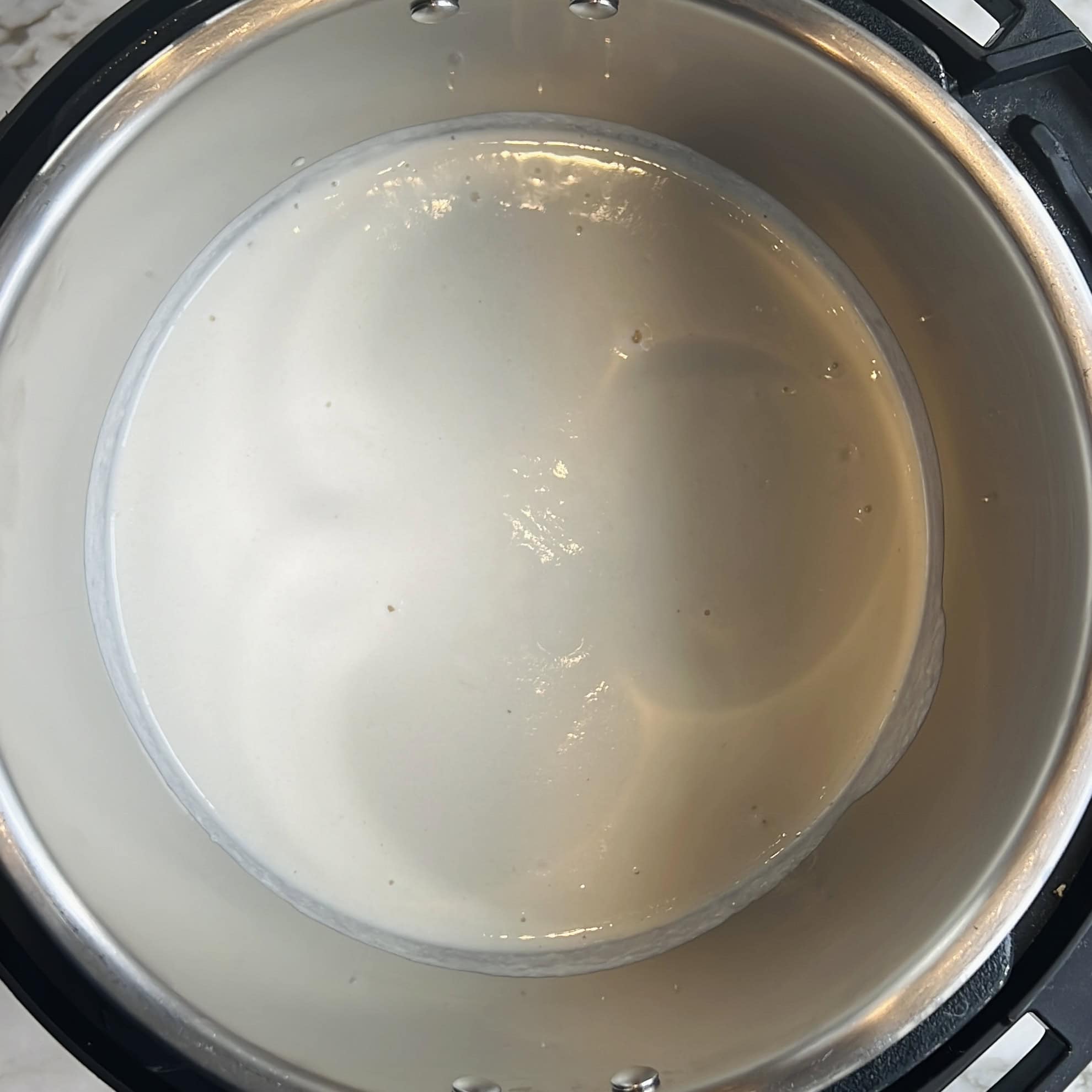 A close-up view of a stainless steel pot containing a smooth, white batter.