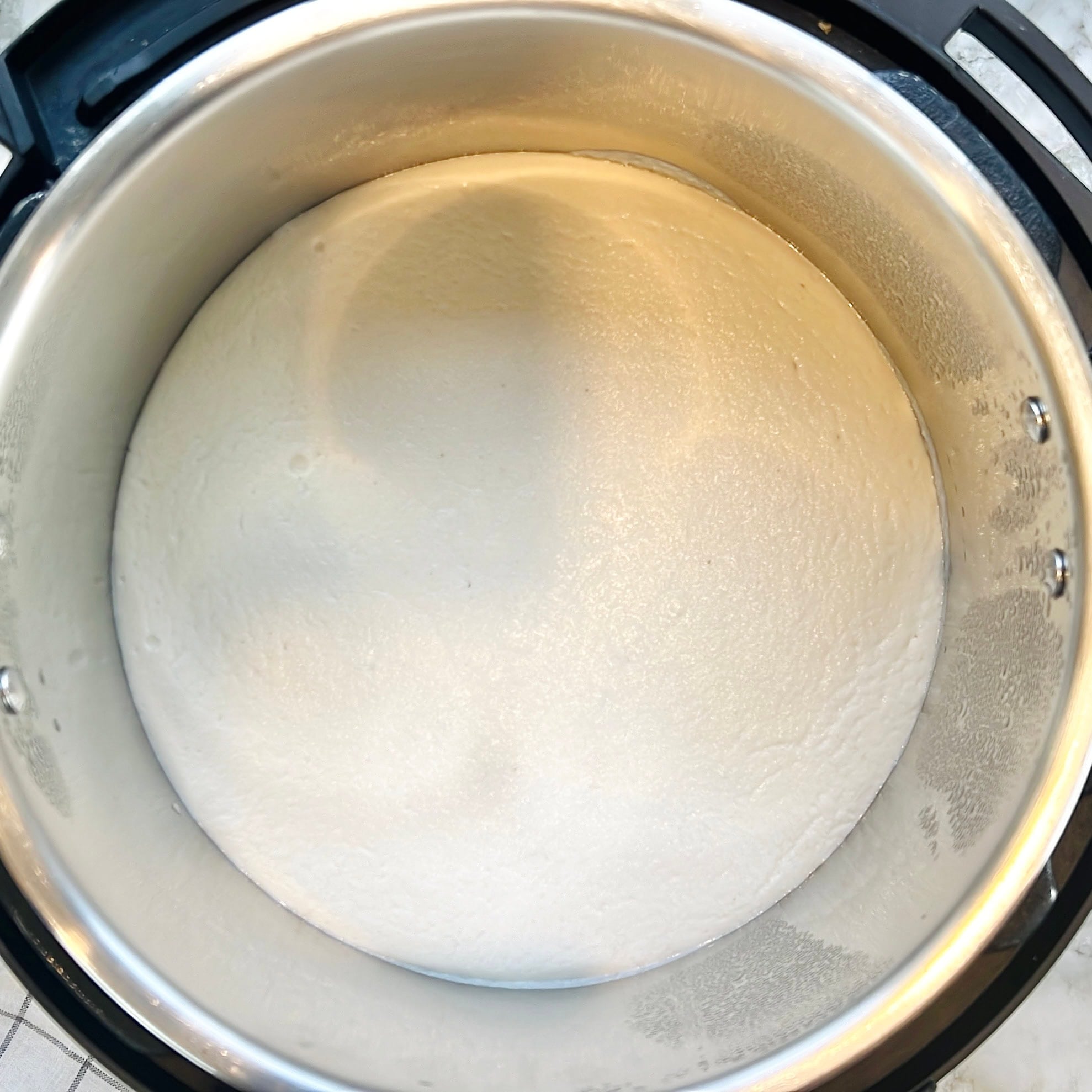 A close-up of risen batter inside a stainless steel pot, in an electric pressure cooker Instant Pot.