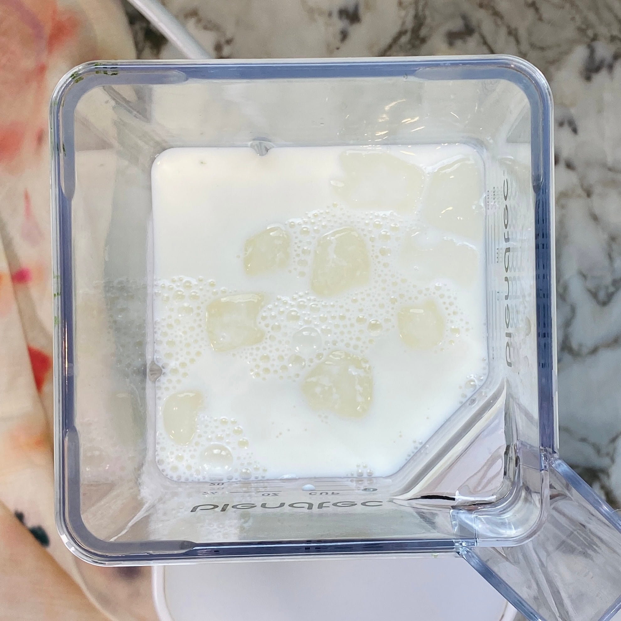 Top-down view of a blender containing milk and ice cubes, placed on a marble counter.