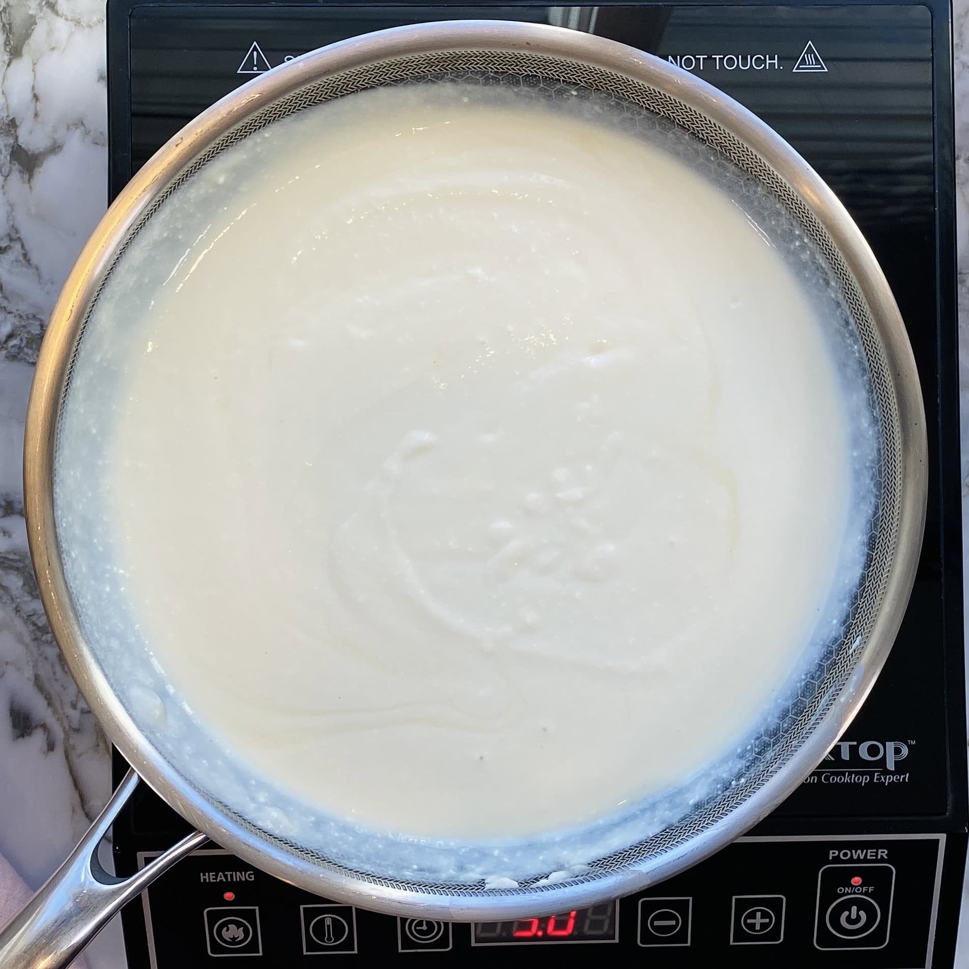 A saucepan filled with white liquid, possibly milk or cream, is heating on an induction cooktop.