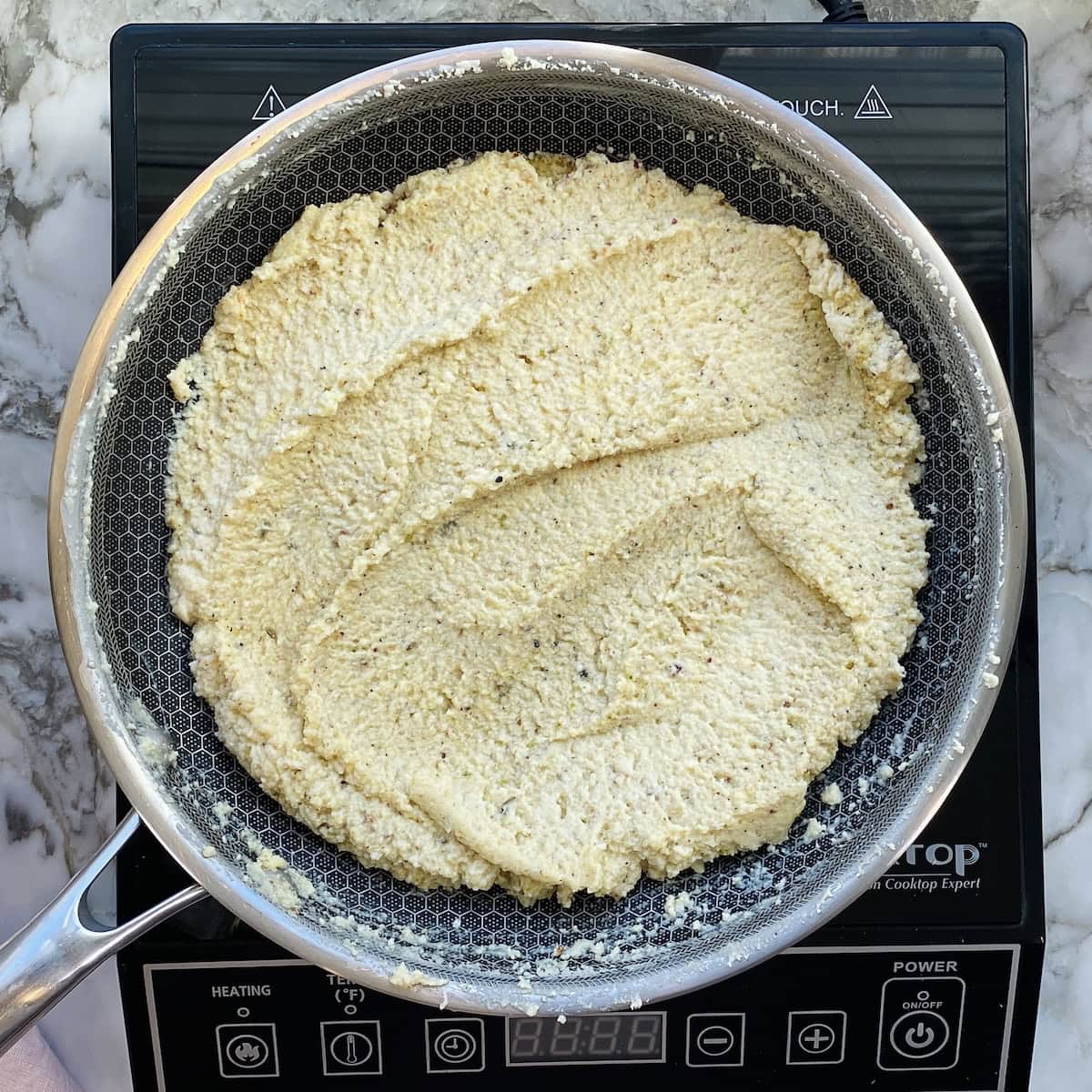 Uncooked flatbread dough spread evenly in a frying pan on top of an electric cooktop.