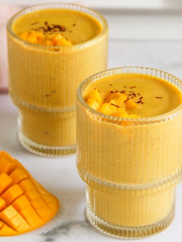 mango thandai served in 2 glasses topped with diced mango and saffron