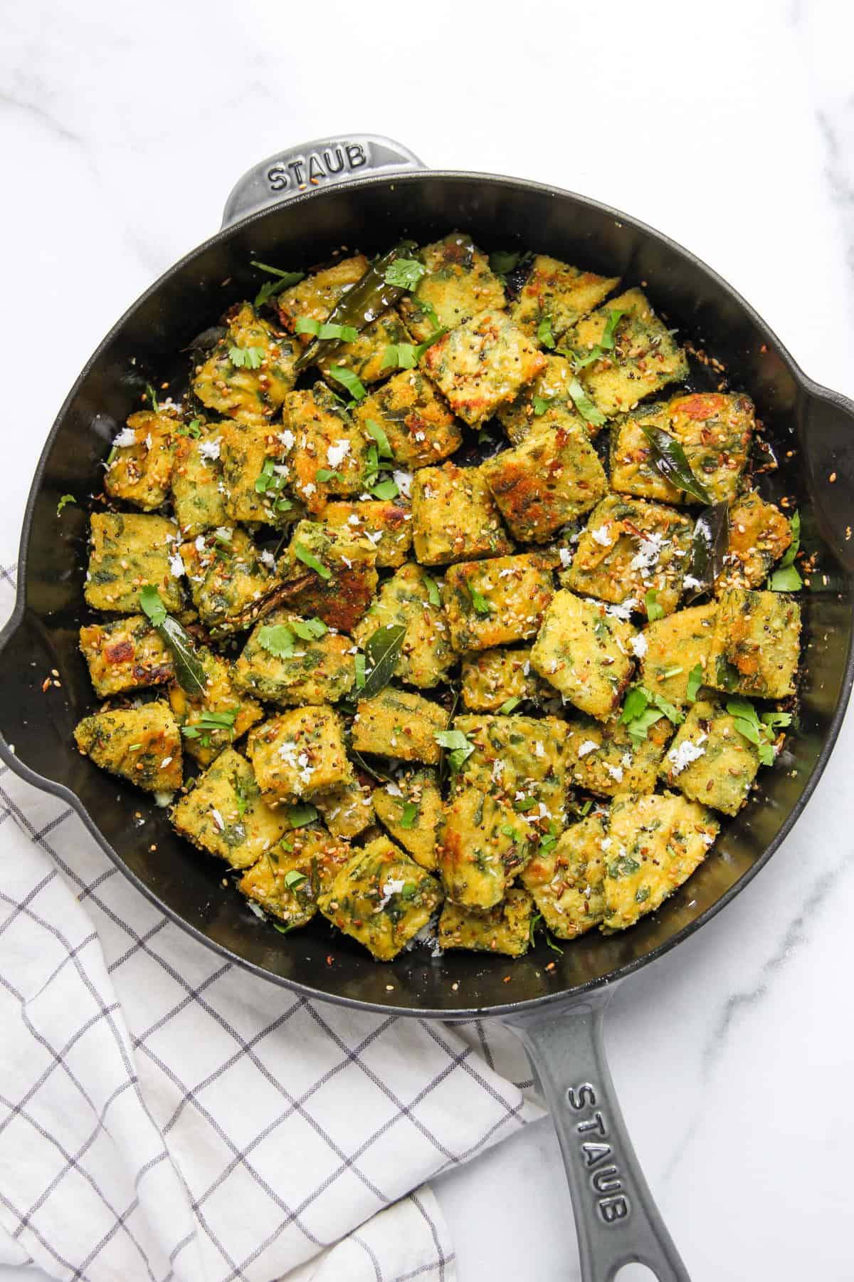 dudhi muthia in a pan garnished with cilantro and grted coconut. 