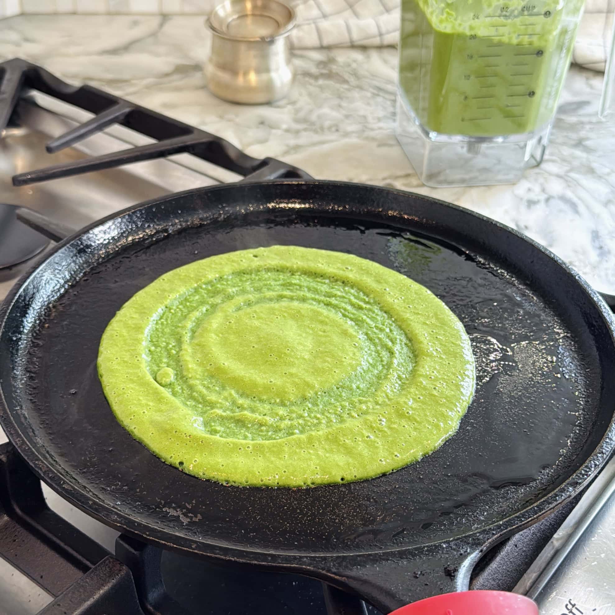 spinach chilla batter spread on a cast iron pan.