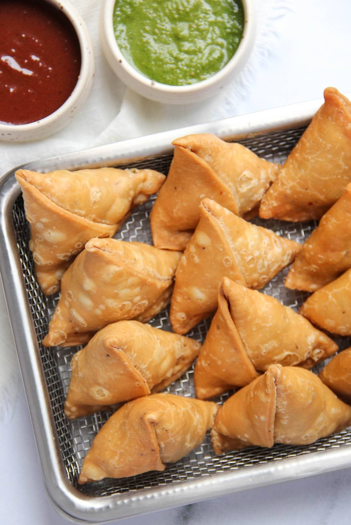 samosas on a stainless steel tray with sweet chutney and green chutney on the side.
