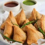 khasta samosas served with fried green chilies and chutneys.