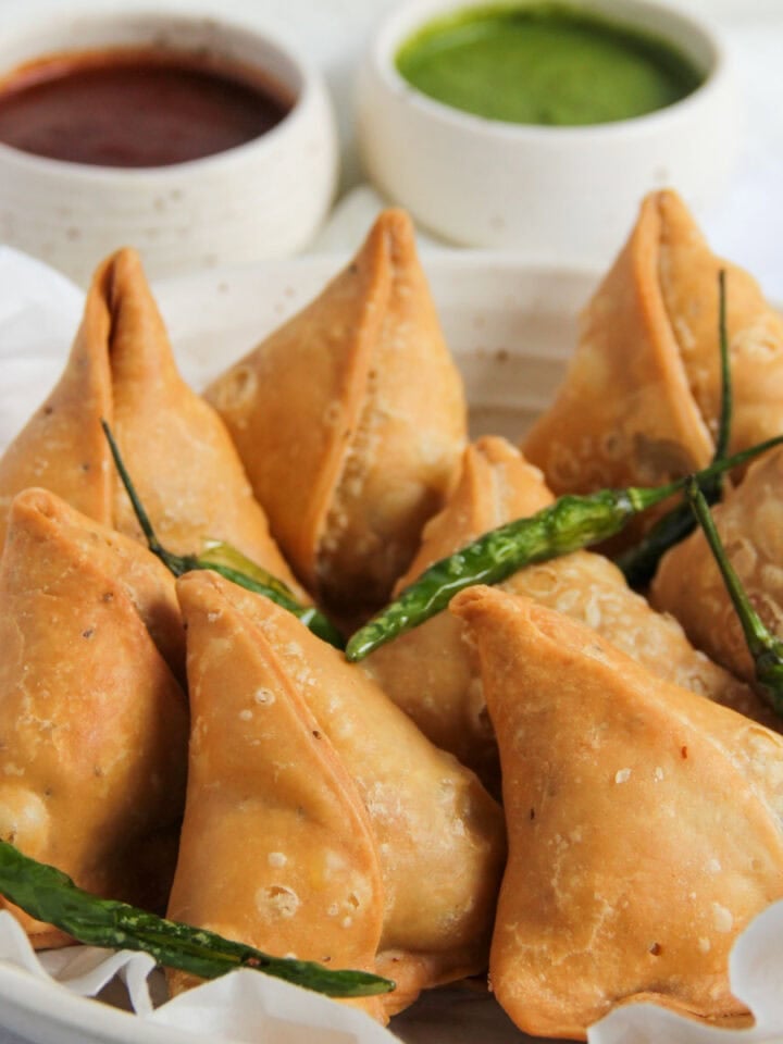 khasta samosas served with fried green chilies and chutneys.