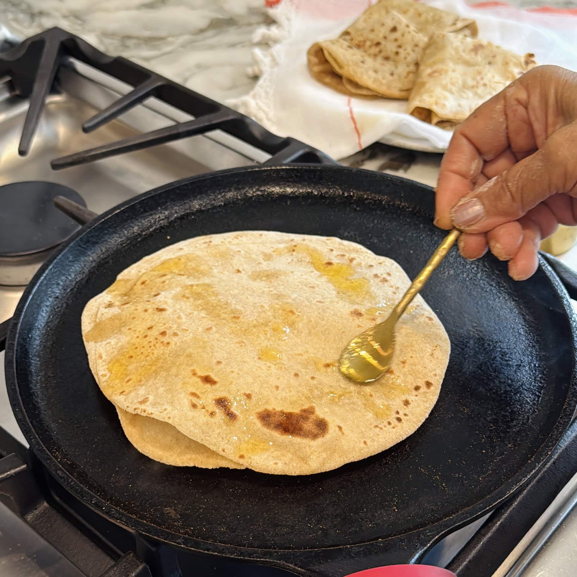 applying ghee to chapati on a cast iron pan.