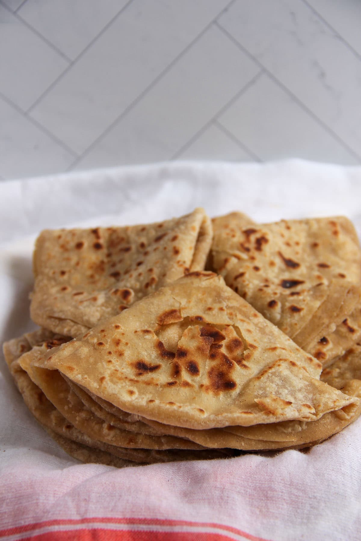 folded chapatis on a white kicthen towel.