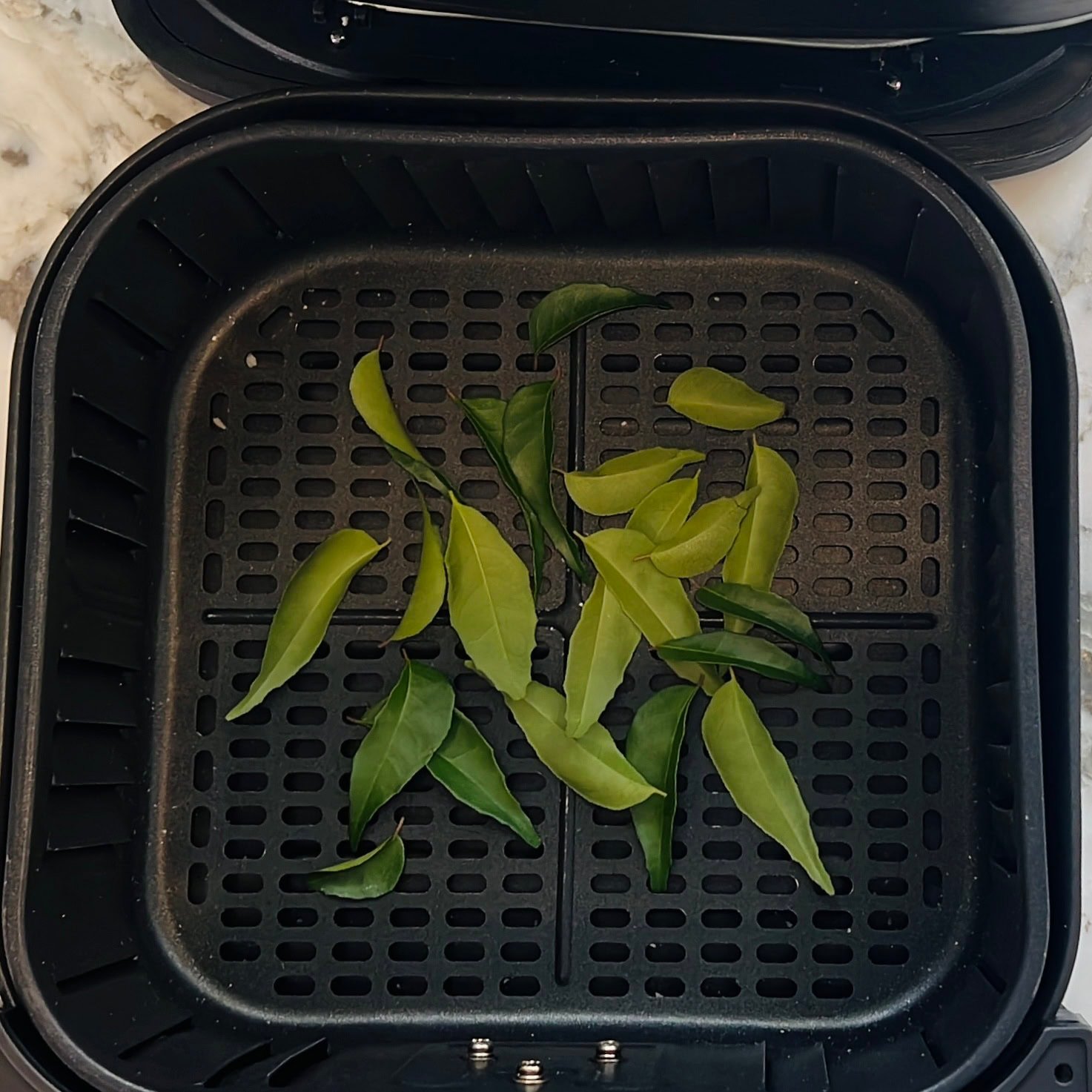 curry leaves in a air fryer basket.
